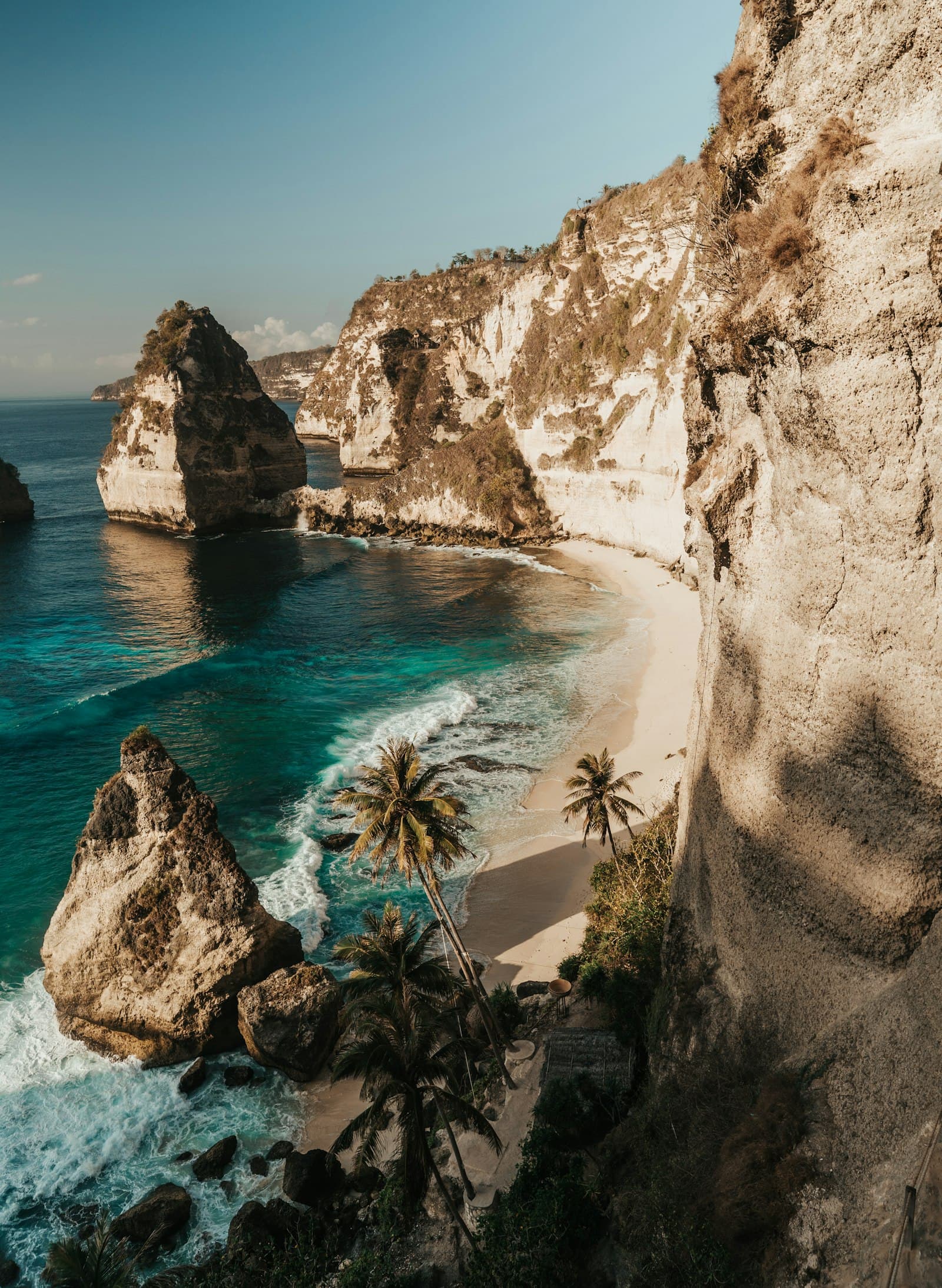 A hidden sandy cove backed by cliffs and palm trees near Bali's southeast coast.