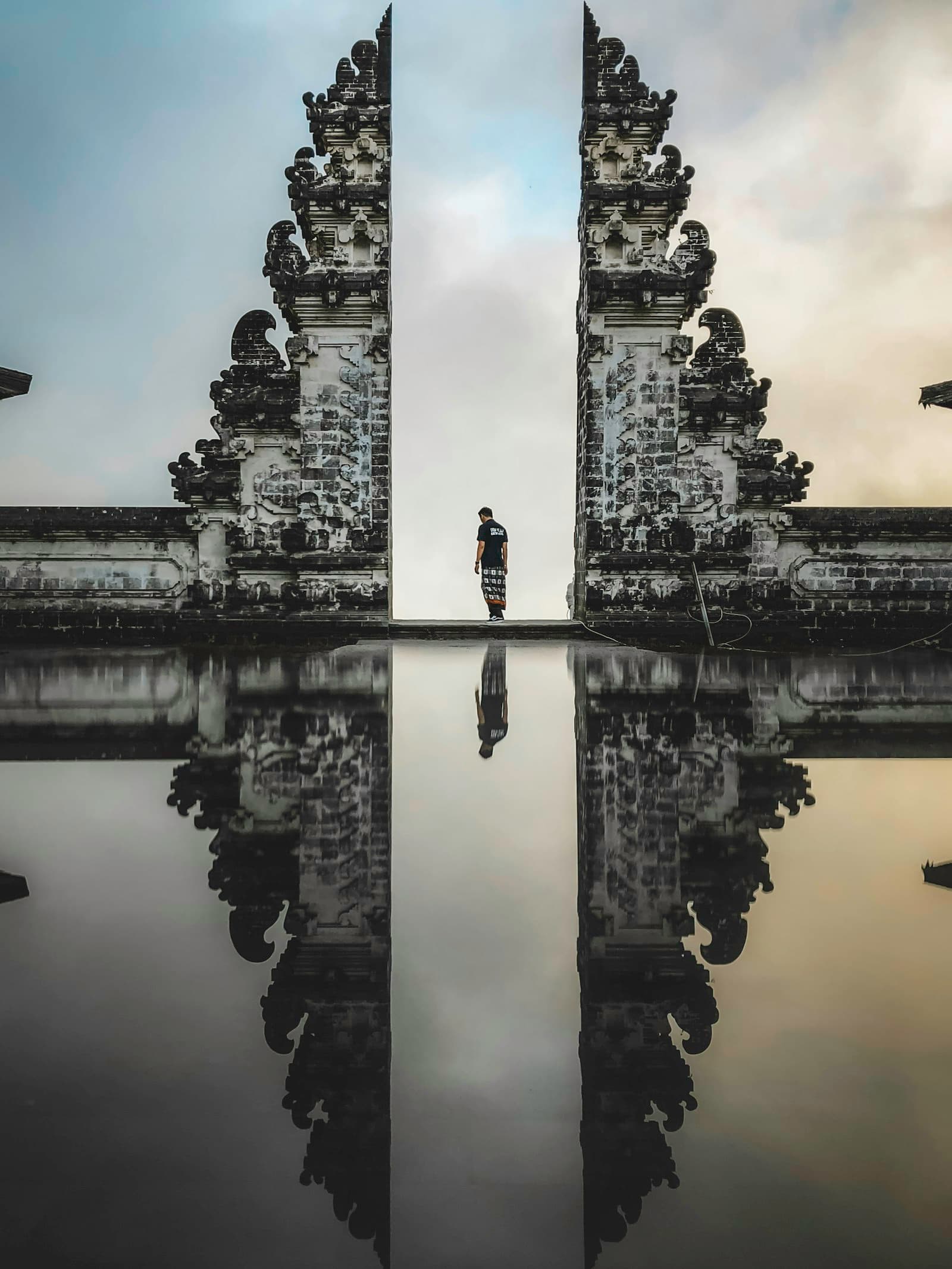 The split gate of Lampuyang Temple framing the sky, with its reflection in still water.